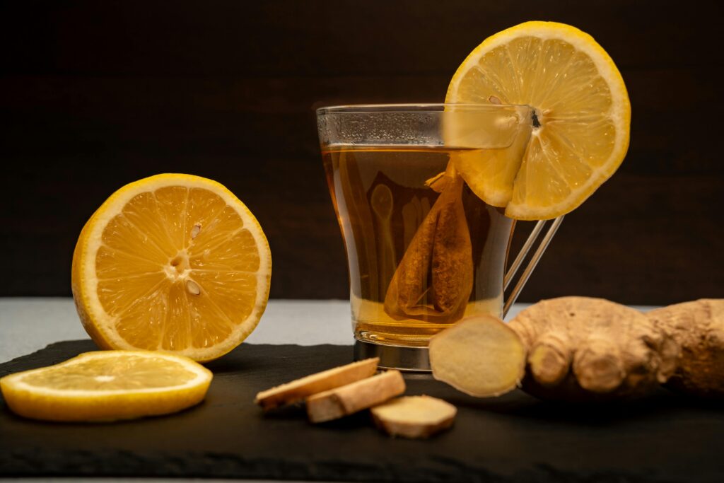A warm cup of lemon ginger tea surrounded by fresh lemon slices and ginger root on slate.